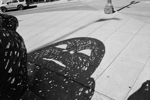 a shadow cast by a sculpture of a baby doll's face on a sidewalk.